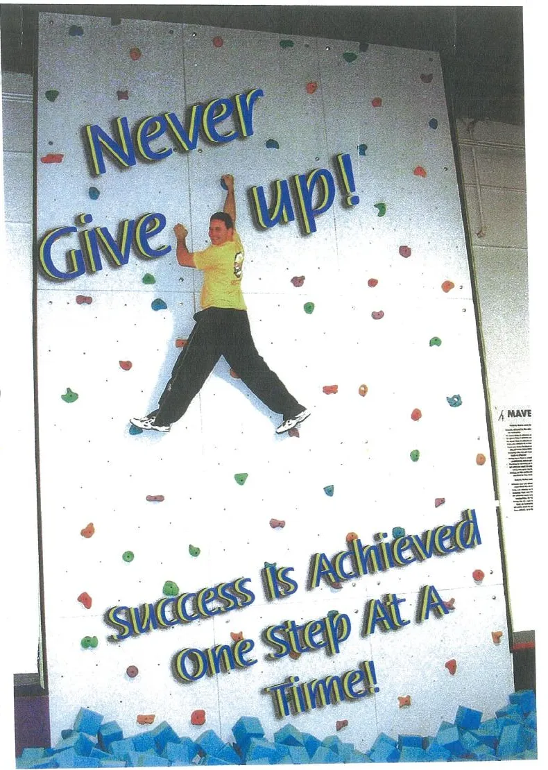 Nick on the Maverick climbing wall under the words Never Give Up